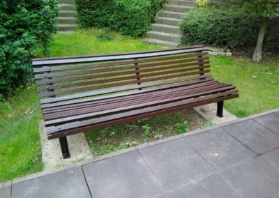 Modern barna lécezett fémvázas pad zöld gyep és gumilapos járda mellett