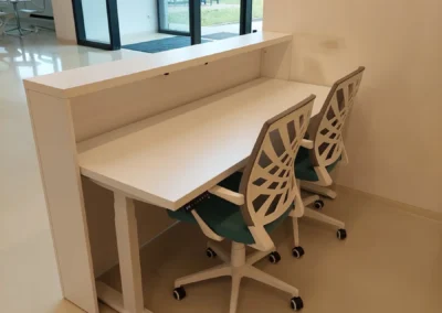 Fehér színű recepciós pult modern irodaszékekkel egy világos irodaház előterében
