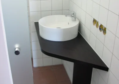ves fekete sarok mosdópult fehér kerek mosdókagylóval, fehér csempézett falnál