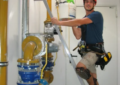 Ipari alpinista beltéri szerelést végez csőrendszer mellett