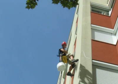 Ipari alpinista ház falán dolgozik vödörrel, homlokzat javítás