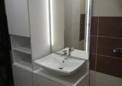 Elegáns fehér fürdőszobai összeállítás fiókos szekrénnyel, állószekrénnyel és LED-es tükörrel.