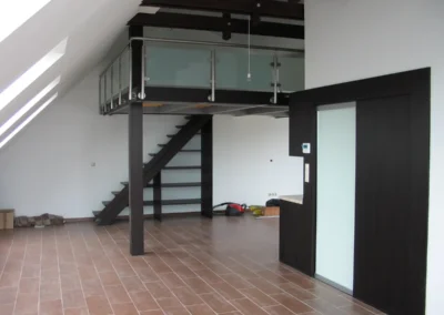 Modern belső galéria üvegkorláttal, sötét acélszerkezetű lépcsővel és tetőtéri ablakokkal
