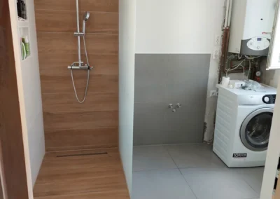 Modern fürdőszoba zuhanyzóval, mosógéppel és szürke padlóburkolattal