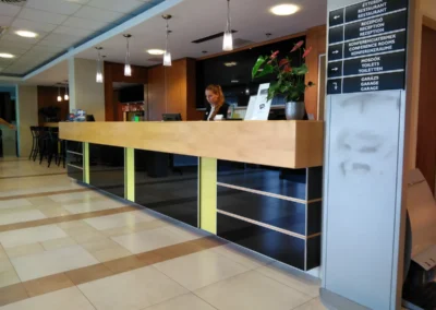 Modern, nagyméretű fa és fekete üvegbetétes szállodai recepciós pult információs táblával